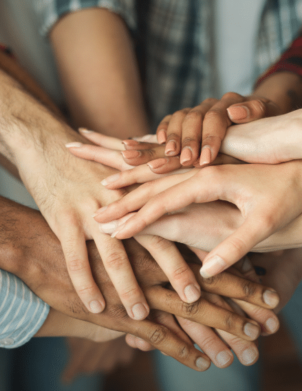 A group of people stack their hands together in the center, showing unity and teamwork. The hands vary in size and skin tone, and some have visible manicured nails.