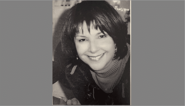 Black and white photo of a woman with short, dark hair, wearing a turtleneck sweater and earrings, smiling at the camera.