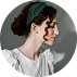 A woman with curly brown hair tied back with a dark green headband is shown in profile. She is wearing a white blouse and looking to the right against a neutral background.