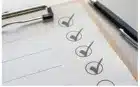 A close-up of a clipboard holding a checklist with several items marked with checkmarks. A black pen lies on the right side of the clipboard.