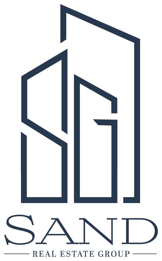 A navy blue geometric logo combines the letters S and G to form a stylized building, thoughtfully reflecting the foundation of emotional and spiritual healing. Below, the text reads SAND REAL ESTATE GROUP in matching navy blue, with thin lines on either side of the words REAL ESTATE GROUP.